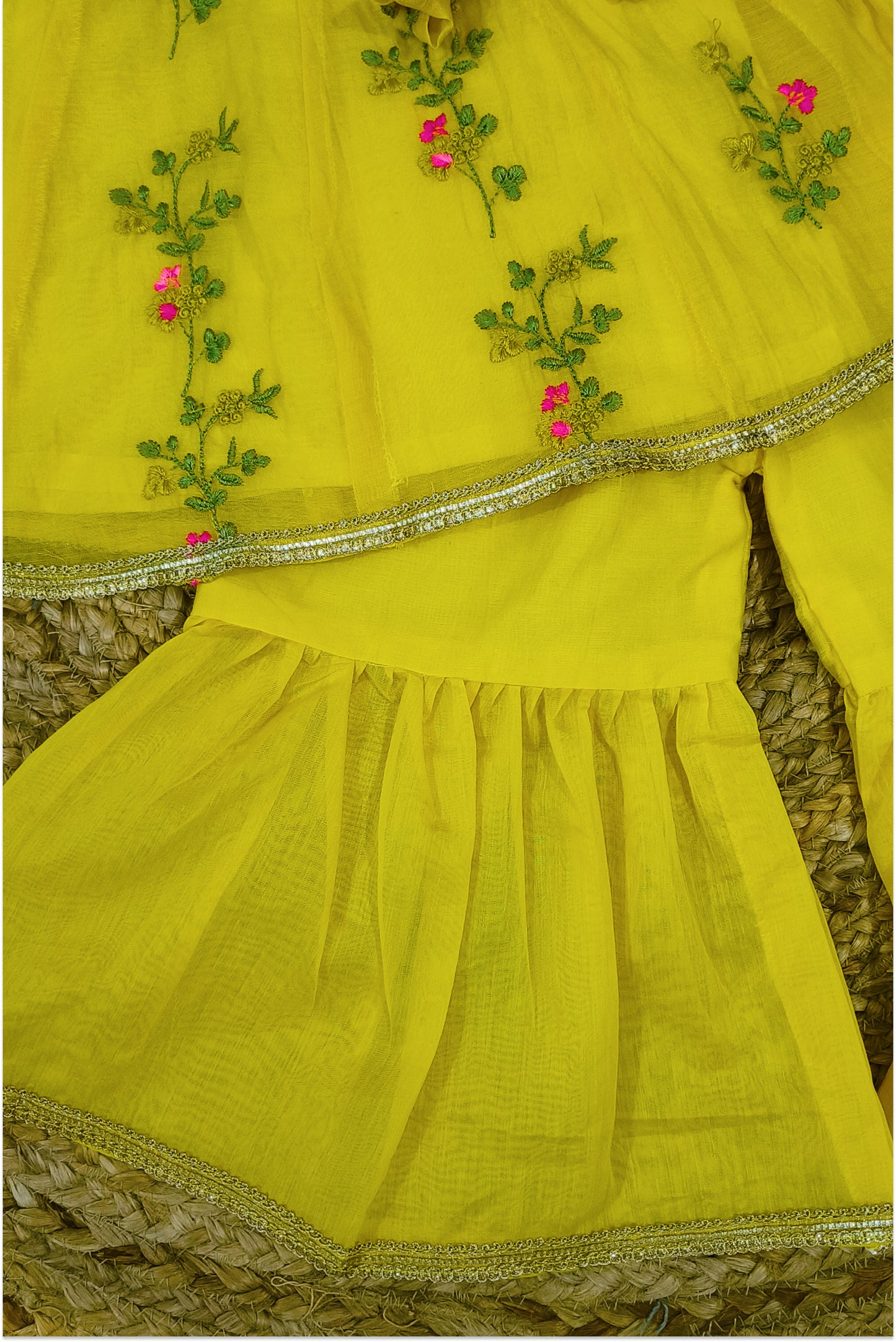 Close up of yellow peplum top showing green vine and pink floral hand embroidery with golden lace trim