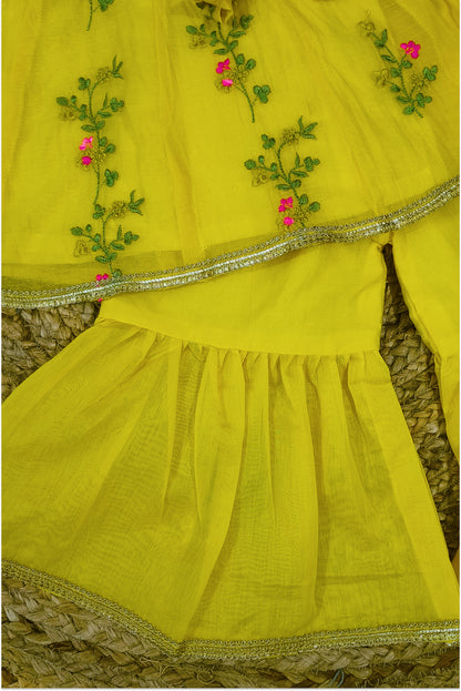 Close up of yellow peplum top showing green vine and pink floral hand embroidery with golden lace trim