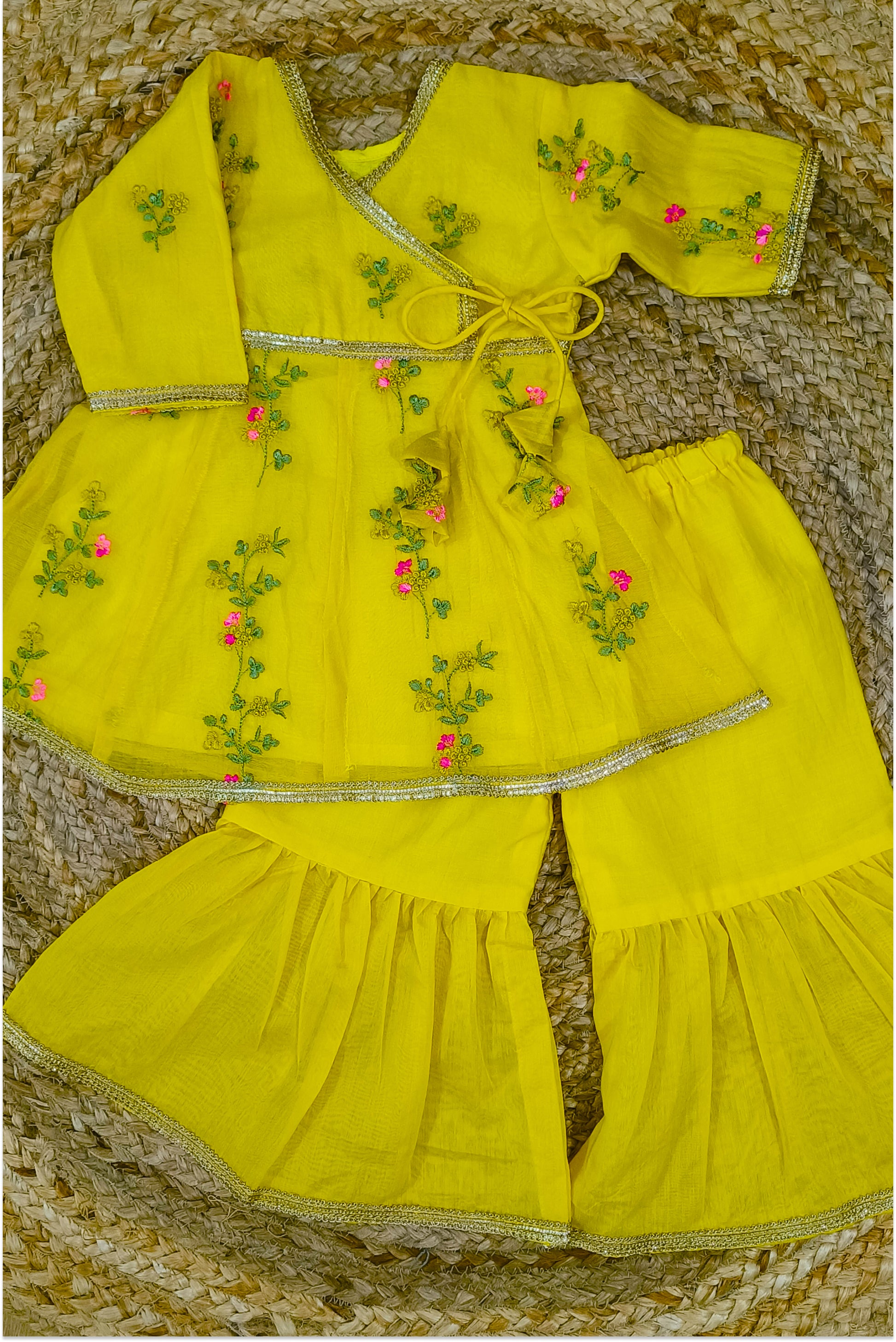 Yellow mul chanderi sharara set flat lay showing peplum top with tie-up, sharara pants, hand embroidery and golden lace